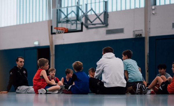 Mehrere Kinder sitzen zusammen auf dem Boden einer Sporthalle