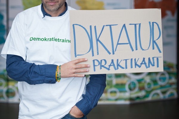 Fatih Çevikkollu hält ein Schild hoch, auf dem "Diktaturpraktikant" steht.