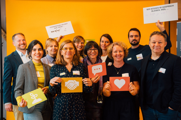 Das Team der Regiestelle Zusammenhalt durch Teilhabe Verschiedene Menschen lächeln und halten Schilder hoch